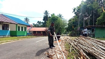 Babinsa dan Warga Bergotong Royong untuk Memperbaiki Kerapian Kampung dengan Membersihkan Kayu untuk Membuat Pagar